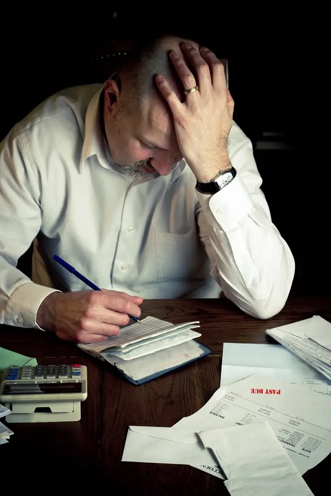 Man stressed about finances with bills and calculator.